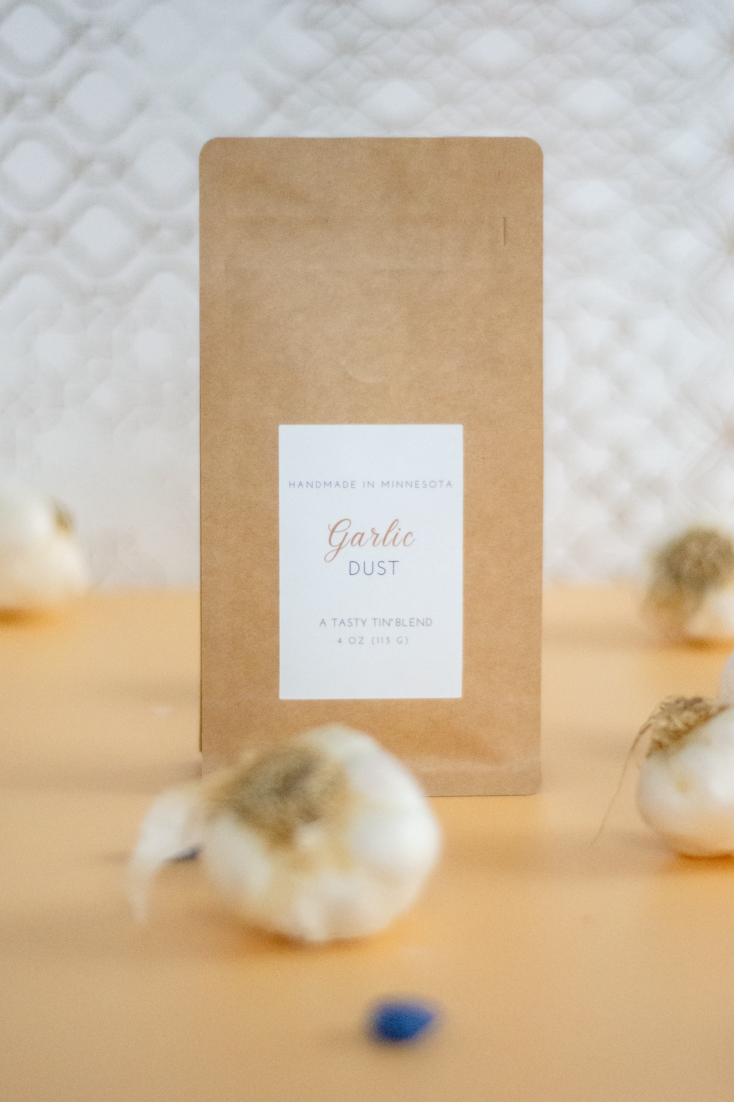 Tasty Tin garlic seasoning refill pouch labeled Garlic Dust surrounded by garlic bulbs on wooden surface