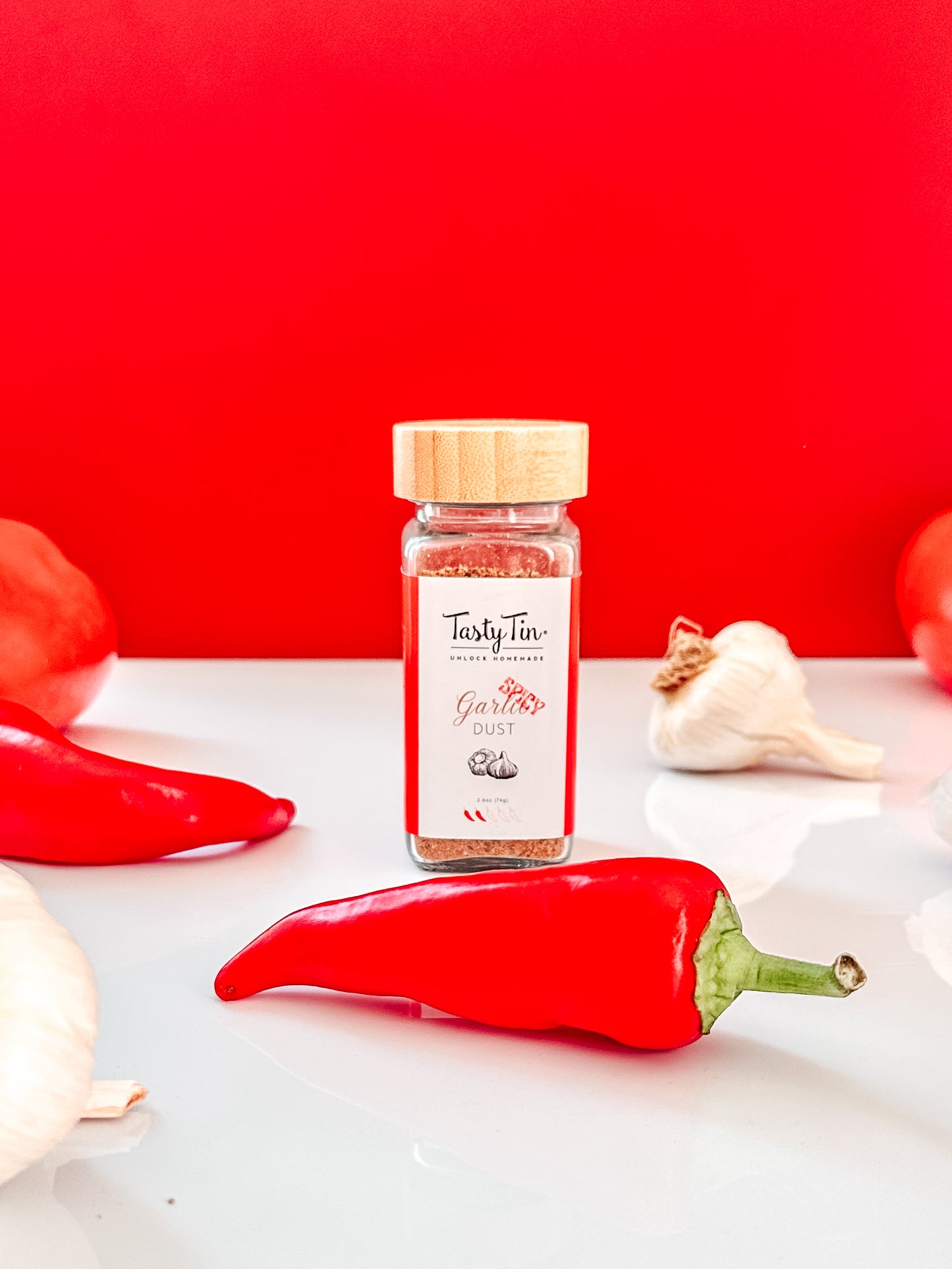 Tasty Tin spicy garlic seasoning shaker with bamboo lid surrounded by red chili peppers and garlic cloves