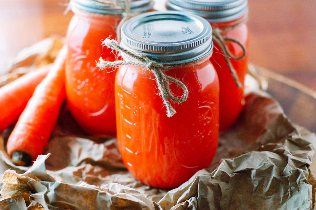 Carrot apple juice in mason jars with twine tide around the side carrots sitting beside them and everything on a crinkly brown paper bag