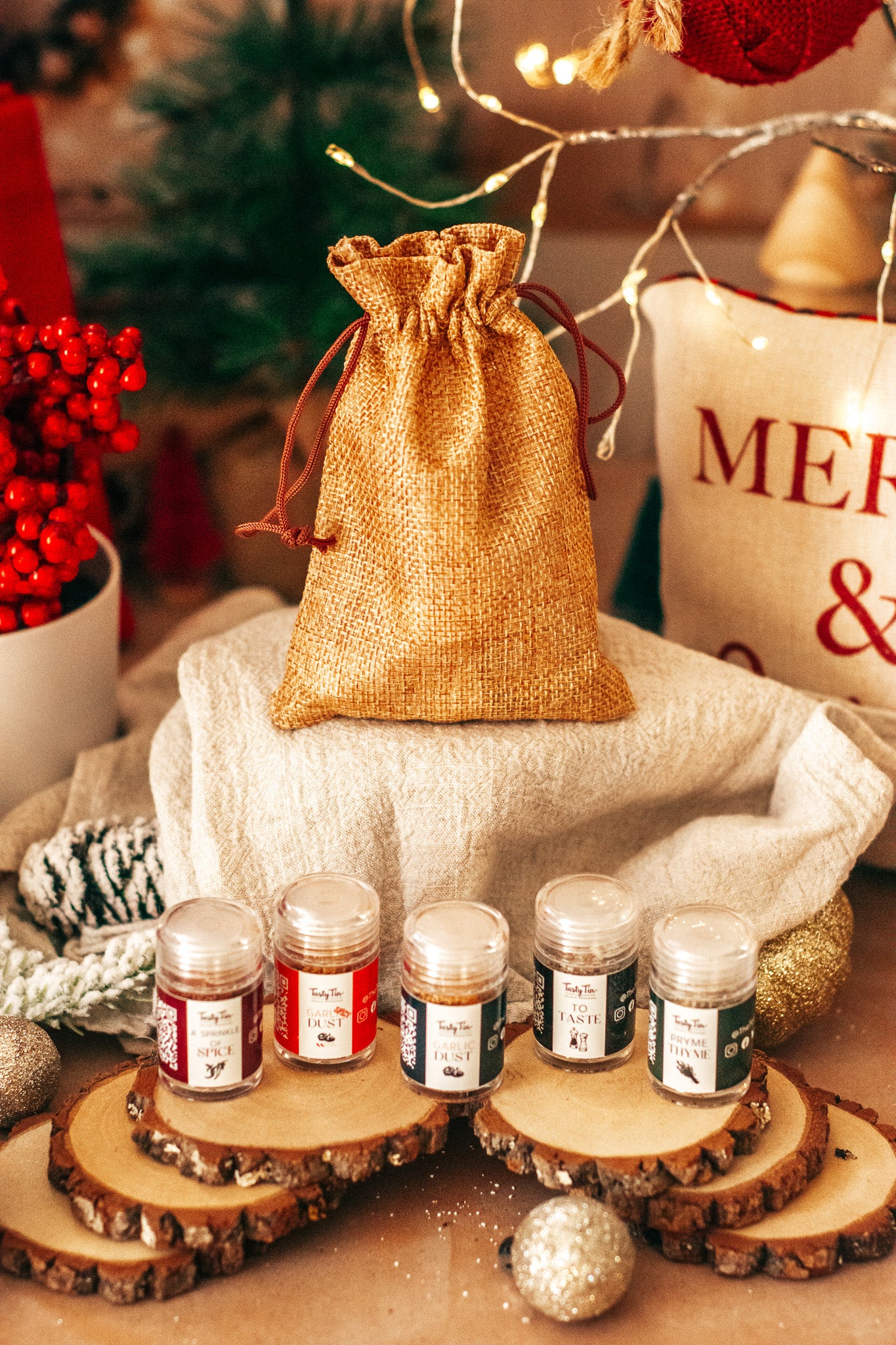 Small jars on wooden coasters with a decorative bag and Christmas decorations in the background