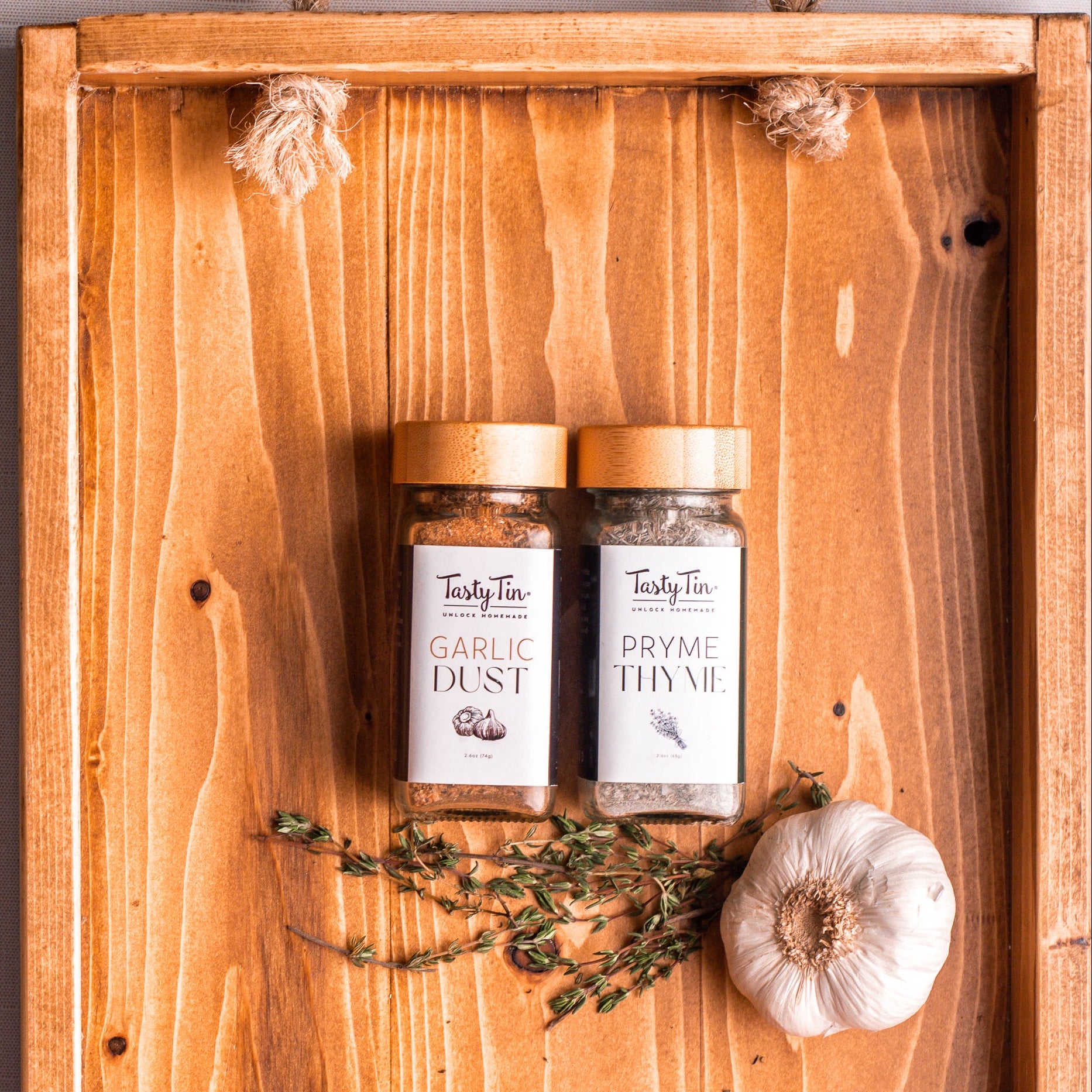 Two jars of 'Garlic Dust' and 'Pryme Thyme' on a wooden board with a white background