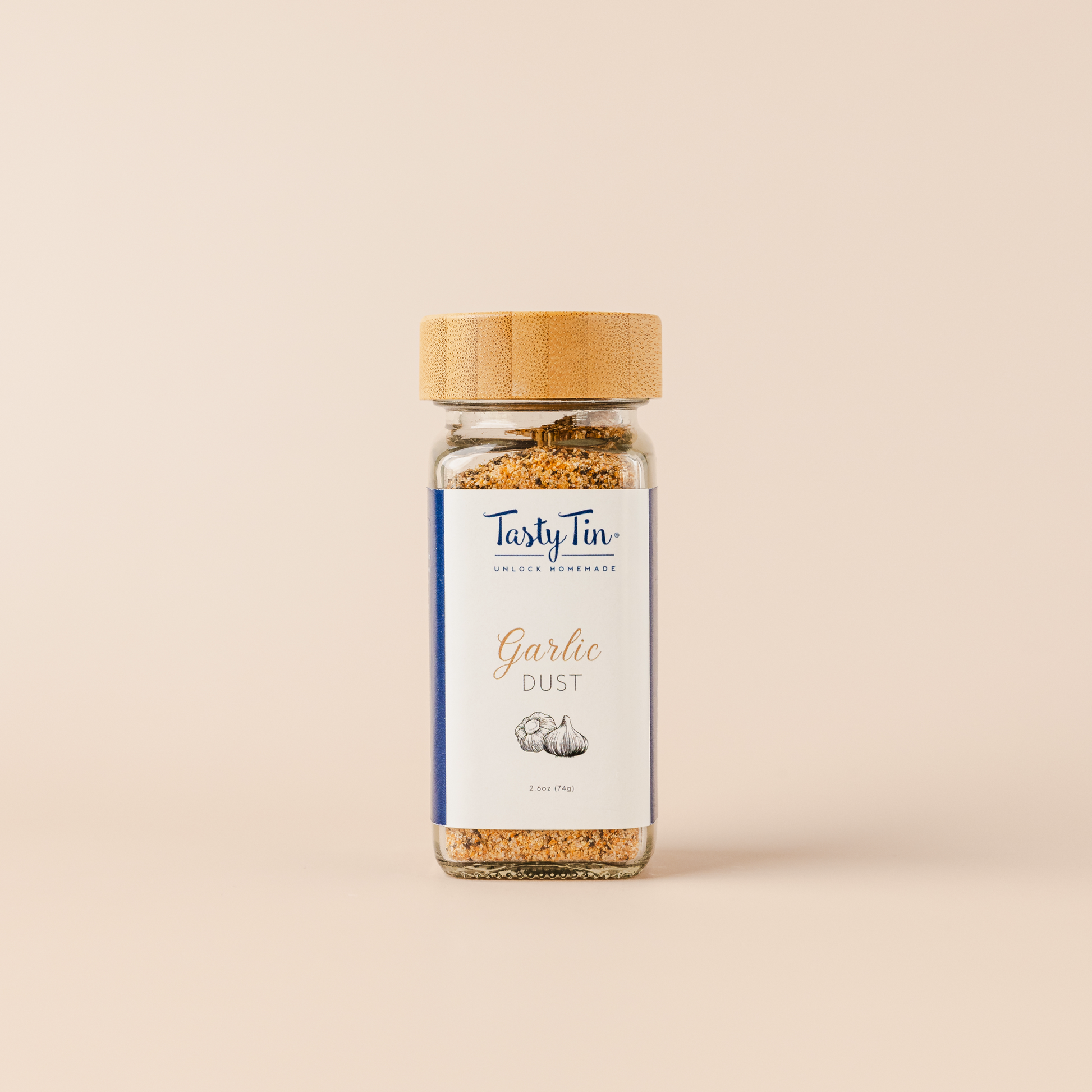 Tasty Tin garlic dust seasoning shaker with clear glass and bamboo lid on beige background
