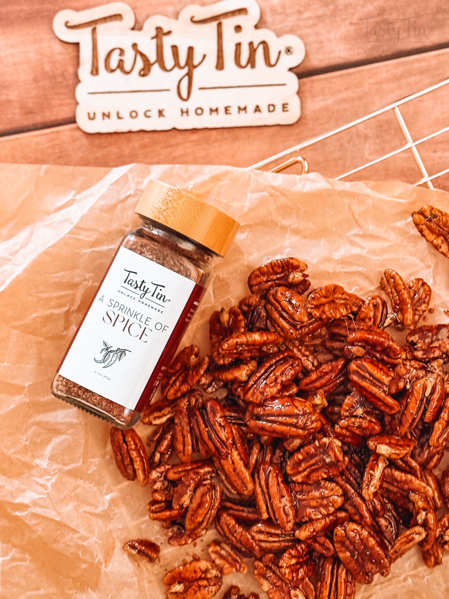 Tasty Tin gourmet spice shaker with a bamboo lid next to a pile of seasoned pecans on brown paper